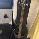 Černá elektrická basová kytara s čtyřstrunným hnedým hmatníkem. Na hlavě je bílé logo Cort a nápis ACTION Bass. Nástroj je opřen o černý softcase.