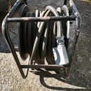Černý kabel namotaný na cirelovém návijáku s kovovým, černým rámem. Rám vykazuje známky opotřebení v podobě odřenin a povrchové koroze. Na kabelu je…