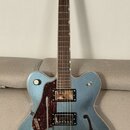 Modrá polodublová elektrická kytara s nápisem GRETSCH na hlavě a spodní části korpusu. Nástroj má dva snímače, červeně vzorovaný pickguard a třicátý…