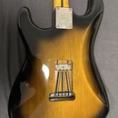 Zadní strana elektrické kytary s tělem v provedení sunburst. Na kovové spojovací desce hředu je vyryto logo "Squier". V zadní části těla je vidět otv…