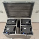 Otevřený hliníkový transportní kufr s vnitřním polstrováním, ve kterém jsou umístěny čtyři černé elektronické jednotky. Každý přístroj má na zadní st…