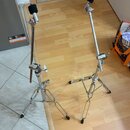 Dvě stříbrné kovové stativy pro mikrofony s černými držáky a černé gumové koncovky na nohách. Stativy jsou rozloženy na podlaze, jeden stojí na dlažb…