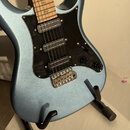 Strunková elektrická kytara s modrým metalizovaným povrchem a černým pickguardem. Nástroj má tři humbuckery, dvě otočné potenciometry a pětipozicovní…