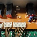 Detailní záběr na oranžovou tiskovanou plošť s elektronickými součástkami, konektory a zapojeným kabelážím. Na desce jsou viditelné nápisy CN201, CN2…