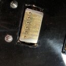 Detail elektrického snímače s kovovým krytem v černé barvě, který je osazen šesti ladicími šrouby. Povrch kovového krytu vykazuje výrazné známky opot…