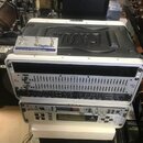 Bílý rack s několika zařízeními. V horní části je umístěn černý plastový kufr s nápisem GATRON a na něm bílý pedalboard DigiTech FOOTSWITCH. Uvnitř r…