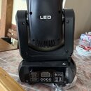 Černý LED světelný efekt typu moving head. Na přední straně je bílý nápis LED a v dolní části se nachází ovládací panel s digitálním displejem a tlač…