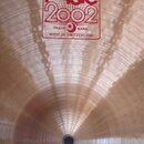 Kruhová kovová činely v bronzové barvě s viditelným broušením povrchu. Uprostřed je červený hranatý nápis PAiste 2002 TRADE MARK MADE IN SWITZERLAND…