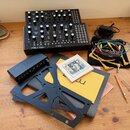 Na fotografii je černý analogový syntetizátor s nápisy MOTHER-32 a moog. Vedle něj leží černý audio rozhraní s logem Focusrite, sada barevných patch…
