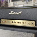 Kytarový zesilovač Marshall Origin 50 v černé texturované krytince se zlatým předním panelem. Na panelu jsou umístěny přepínače, ovládací knofíky s n…