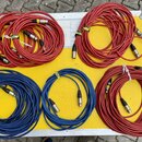 Pět svátků audio kabelů s XLR konektory, položených v otevřeném transportním kufru. Kabely jsou v červené a modré barvě, část z nich má bílé papírové…