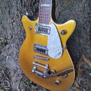 Zlatá elektrická kytara s hnědým hnedým hmatníkem a bílo-perleťovým plechtrem. Na těle je vidět nápis bretsch. Kytara má dva humbuckery, chromovaný m…
