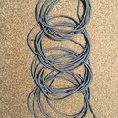 Šedý elektrický kabel svázaný do několika volných smyček. Na koncích jsou viditelné odkryté měděné vodiče. Kabel nemá žádné čitelné nápisy ani značky.