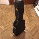 Černý tvrdý kufr na kytaru s bílým lemováním hran. Kufr má kovové zapínání a úchyt na straně. Povrch je v dobrém stavu bez viditelných poškození.