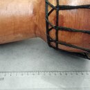 Dřevěný buben s hnědým povrchem a černým provázkovým napínacím systémem. Vedle nástroje je položeno pravítko s nápisem KOH-I-NOOR HARDTMUTH. Na povrc…