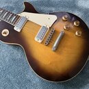 Elektrická kytara s tónem těla v hnědém sunburst provedení a krčkem z tmavého dřeva. Nástroj má dva snímače s bílými rámečky, bílý plecháč a čtyři zl…