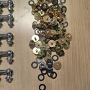 Na fotografii je vidět sada kovových součástek, pravděpodobně ladicích mechanismů a příslušenství. Vlevo jsou vyrovnány chromované kovové části s kul…