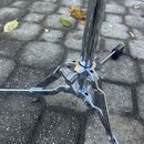Detail spodní části chromovaného stojanu s rozkládacími nohama. Na jednom z kovových prvků je vidět nápis "Mapex". Povrch je lesklý, s mírnými známka…
