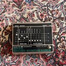 Stříbrný efektový pedál s černým ovládacím panelem. Na spodní části je nápis ELECTRO HARMONIX MADE IN USA BASS MICRO SYNTHESIZER. Panel obsahuje něko…