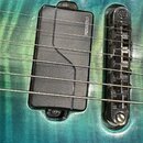 Detail elektrické kytary s modrým probarvovaným povrchem. Na těle je vidět černý humbucker s nápisem FISHMAN a černý strunový můstek. Povrch kytary v…