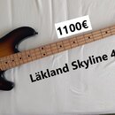 Elektrická basová kytara s tělem v barvě sunburst a světlou hnedou hmatníkem. Na hlavě je vidět logo LAKLAND a nápis skyline series. Tělo má dva čern…