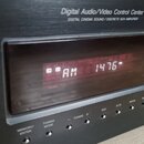 Černý Digital Audio/Video Control Center s nápisem DIGITAL CINEMA SOUND / DISCRETE 5CH AMPLIFIER. V displeji svítí červeným text AM 1476. Pod displej…