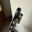 Fotografie zachycuje zadní stranu hlavy kytary v černé barvě. Jsou vidět kovové ladicí mechanismy stříbrné barvy. Na jednom z mechanismů je čitelně n…