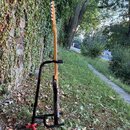 Na fotografii je elektrická kytara s přírodním dřevěným krčkem a tmavým tělem, umístěná na černém stojanu. Kytara má bílé ladičky a světlou hmatnici.…
