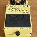 Žlutý kytarový efekt s nápisy SUPER Over Drive a SD-1. Na černém spínacím pedálu je vyražené logo BOSS. Zařízení vykazuje viditelné opotřebení v podo…