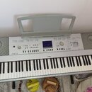 Digitální klavír v dřevěném rámu s šedým ovládacím panelem a přívodním stojanem na noty. Na panelu je vpravo nápis „GrandPiano“ a uprostřed nad kláve…