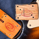 Detailní pohled na spojovací část krku a těla elektrické kytary. Na dřevě v obou částech je červený razítkový nápis CUSTOM SHOP FENDER USA s logem ky…