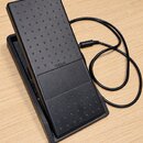 Černý sustain pedál z plastu s protiskluzovou texturou v podobě drobných výstupků. Uprostřed je vidět bílý nápis YAMAHA. K pedálu vede černý kabel s…