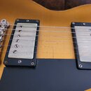 Detail elektrické kytary v žlutém provedení s černým plechtrátorem. Jsou vidět dva humbuckery s bílými kryty a kovovým mostkem. Na povrchu laku jsou…