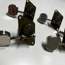 Čtyři kovové ladicí mechanismy s chromovanými knoflíky. Mechanizmy mají mosazný nebo pozlacený povrch s viditelným opotřebením a oxidací. Na dílech n…