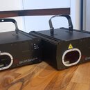 Dvě černé hranaté elektronické jednotky s kovovými rukojtěmi. Na přední stranách jsou kulaté otvory a žluté varovné trojúhelníky. Jsou zde nápisy WIC…