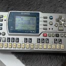 Stříbrný sekvencer Yamaha QY100 s LCD displejem a numerickou klávesou. Na horní straně je nápis YAMAHA a pod displejem text MUSIC SEQUENCER QY100. Za…