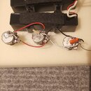 Dvě černé humbuckery s černými kryty. K nim jsou připojeny potenciometry a kondenzátor s nápisem A250K. Celý soubor komponentů leží na bílém polystyr…