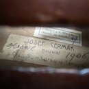 Detail vnitřku dřevěného nástroje s dvěma papírovými štítky. Na horním menším štítku je nápis „Opravil J. B. HERCLÍK houslar, Ml. Boleslav“ a modré č…