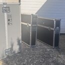 Čtyři transportní flightcasey různých velikostí s kovovými hranami a zámky. Největší šedý case má nápis PROPERTY OF PHILIPS EUROSERVICE DEPOSIT: EURO…