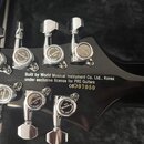 Zadní strana hlavy černé kytary s chromovanými ladicími kolíky značky GOTOH. Na zadní straně hlavy je bílý nápis: Built by World Musical Instrument C…