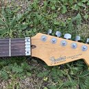 Hlava a hриф elektrické kytary s tmavým hmatníkem. Na hlavě je vidět logo Fender, nápis STRATOCASTER a MADE IN U.S.A., dále označení SERIAL NUMBER N1…