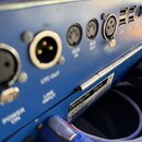Detail zadní strany modrého elektronického zařízení s několika konektory. Jsou zde viditelné porty s popisky LTC OUT, MIDI IN, MIDI OUT a LTC IN, dál…