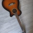 Akustická kytara s vyřezem v těle a tmavě hnědým přechodem k okrajům (sunburst). Na hlavě je viditelné logo "Faler". Nástroj vykazuje běžné známky po…