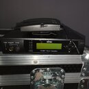 Černý přístroj s nápisem MIPRO a označením M1-808T Stereo Transmitter. Na přední straně jsou umístěny zelený LCD displej, ovládací prvky a konektor p…