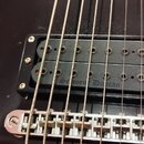 Detail elektrické kytary s tmavým povrchem. Je zde vidět humbucker snímač v černém rámečku s nápisem Seymour Duncan. Pod snímačem je umístěn kovový s…