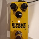 Žlutý kytarový efekt s nápisem RIVULET CHORUS. Na horní straně jsou tři černé otočné knoflíky s popisky RATE, WIDTH a INTENSITY. V dolní části je kov…
