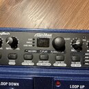 Modrý looper značky Digitech s názvem JamMan STEREO. Zařízení obsahuje několik ovládacích knoflíků (LOOP LEVEL, RHYTHUM LEVEL, MIC LEVEL, INST LEVEL)…