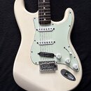 Bílá elektrická kytara s tvarem Stratocaster a světle zeleným pickguardem. Nástroj má tři snímače, jeden z nich je v pozici hradla humbucker. Na ovlá…