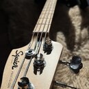 Hlava basové kytary z přírodního dřeva s nápisem Squier by Fender a označením PRECISION BASS. Na hlavě jsou vidět čtyři chromované ladičky, z nichž d…