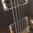 Detail černé elektrické kytary se dvěma humbuckery v chromovaných rámečcích. Horní snímač má na povrchu bílý nápis INFI, dolní snímač má nečitelný ná…
